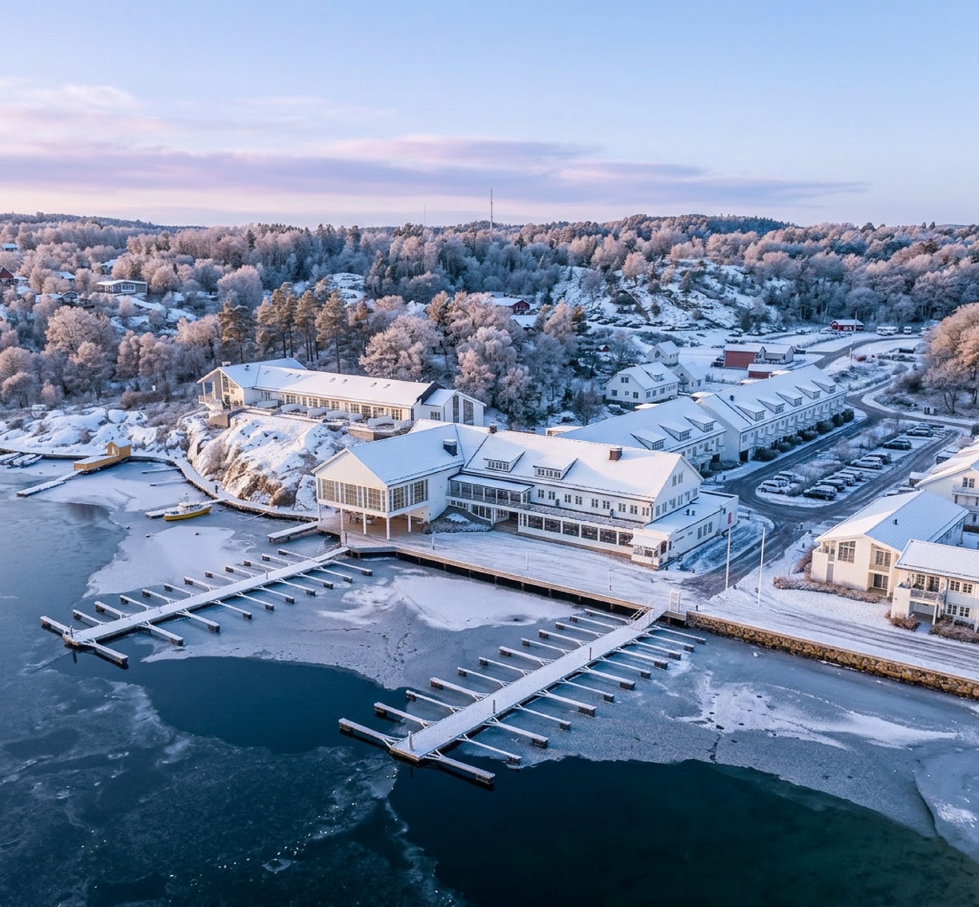 Havna Hotel & Sjøbad i vinterdrakt sett fra luften, med snødekte brygger og isbelagt havn